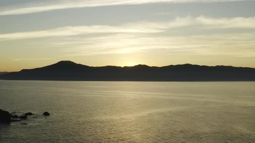 Beautiful aerial drone view sunset golden warm colors over the ocean and mountains on the horizon.