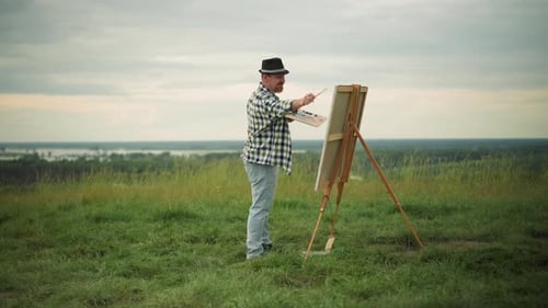 Artist in Hat and Checkered Shirt Painting in a Peaceful Grass Field