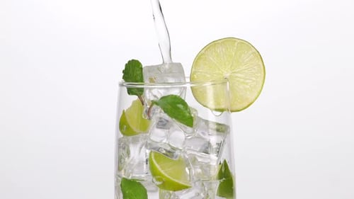 Close Up Of Fresh Lime Soda Being Poured Into A Glass With Mint, Sliced Lime, And Ice