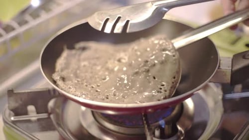 Caucasian right hand flips pancake in skillet with metal tong, slowmo close up