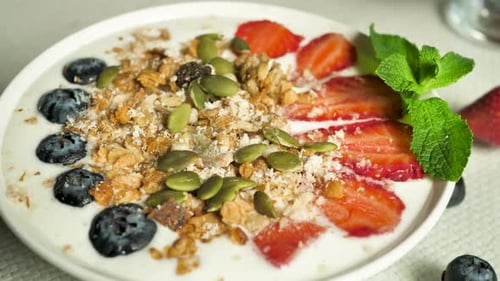 Sprinkle shelled green pumpkin seeds into granola with strawberries and blueberries in fresh yogurt