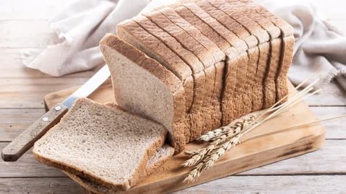 Loaf of sliced wheat bread on wooden board
