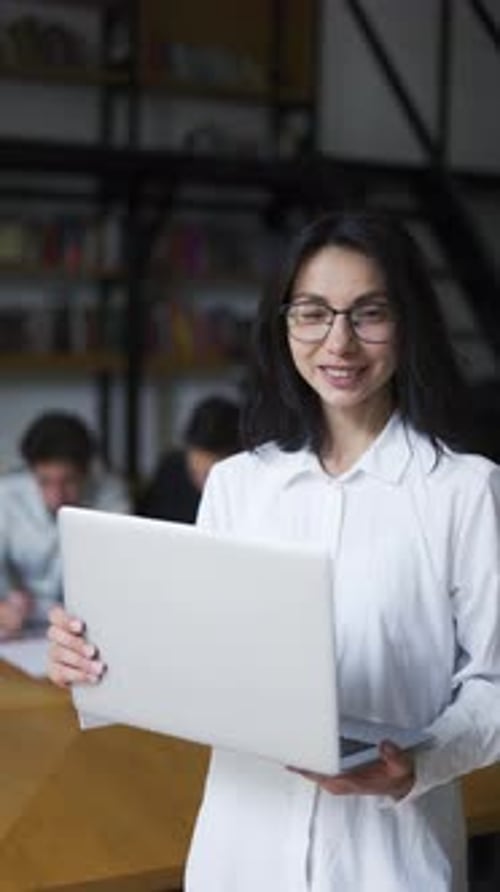 Porträt, lächelnde Frau, Wirtschaftsstudentin, Lehrerin mit Brille, Wissenschaft, posiert am Schreibtisch und Laptop in der Bibliothek