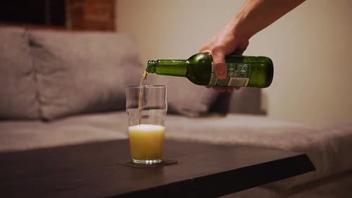 man's hand takes a bottle of beer and pour into a glass, close-up shot