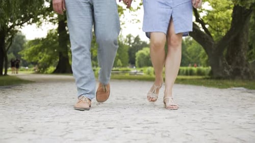 A Caucasian Couple Walks Down a Path in a Park on a Sunny Day Front Closeup on the Legs