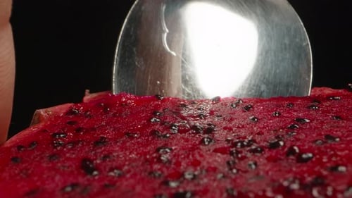 I scoop out the red pulp from the pitahaya with a spoon. Dolly slider, extreme close-up.