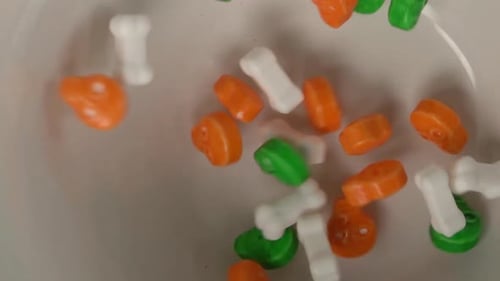 Extreme close up of bones and skulls shaped candy falling on a plate.