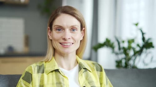 Close-up of caucasian adult woman looking at camera and smiling while sitting on sofa in living room