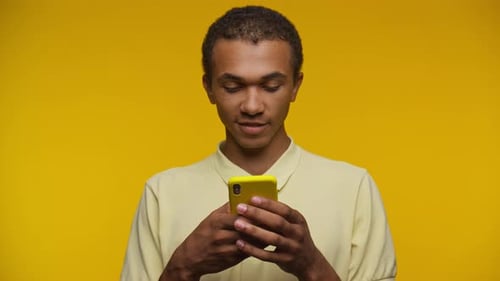 Young Adult Using Cellphone on Yellow Background