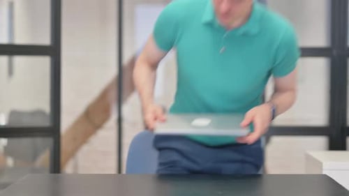 Young Adult Starts Laptop at Office Desk