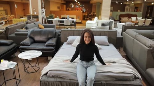 A Woman Tests Beds at a Furniture Store to Show Bedding Options