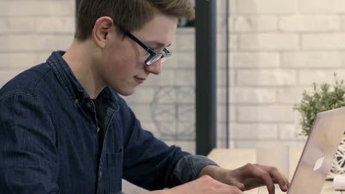 Teen using a Laptop Indoors Near a Brick Wall