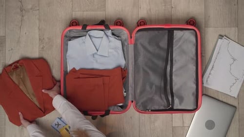 A Woman Fills a Suitcase with a Laptop Documents and a Passport of Top View