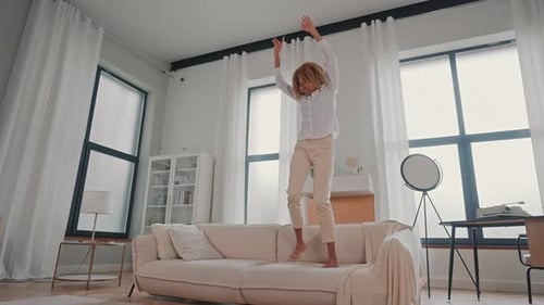Woman Joyfully Dances on Sofa in Living Room