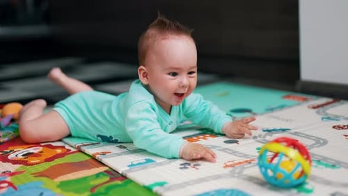 Active baby in blue clothes lies on a colorful mat. Funny kid is happy about a toy in front of him.