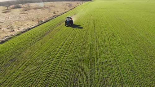 Farmer with Agricultural Machinery Fertilizing Agricultural Field in Spring Time Tractor Spreads