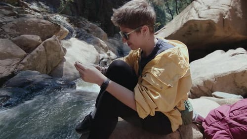 Girl Resting on Mountain Riverbank and Using Phone