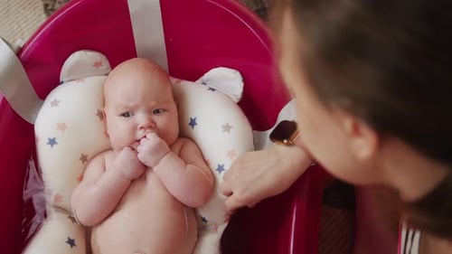 Mother Bathes Her Baby in Pink Bathtub Top View