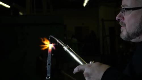 Man Using Blowtorch to Heat Metal in Dark Setting