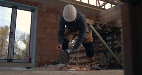 Worker using angle grinder on brick in industrial setting, sparks flying in construction site