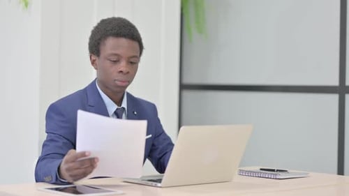African Businessman Celebrating Success while Reading Documents in Office