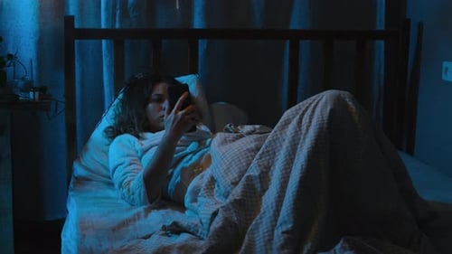Young Woman Lying in Bed Using Smartphone