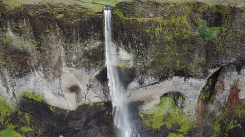 Aerial flyover view of waterfall flowing over cliff / Kirkjubaejarklaustur, Iceland