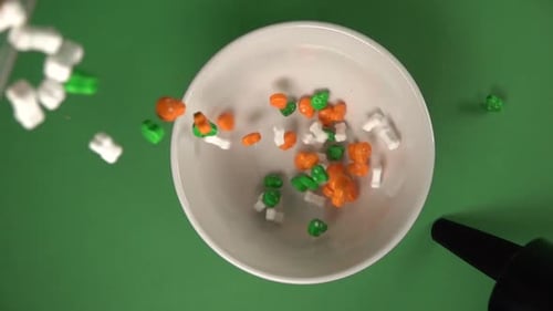 Zenith view of skulls and bones shaped candy slowly falling on a plate from top.