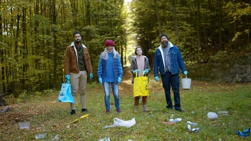 Diverse volunteers smile after cleaning forest waste in community service
