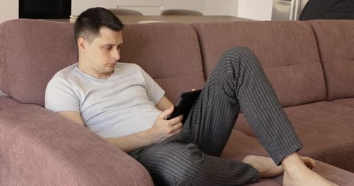 Man Relaxing on Couch Using Tablet Device
