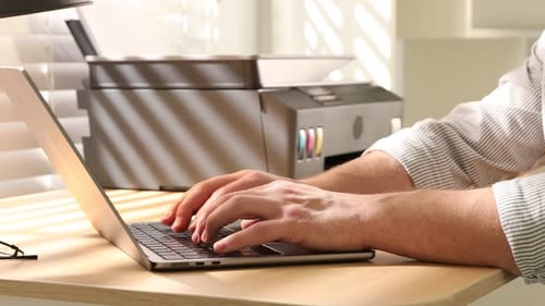 Hombre usando la impresora mientras trabajaba en una computadora portátil en un escritorio de madera en el interior, primer plano