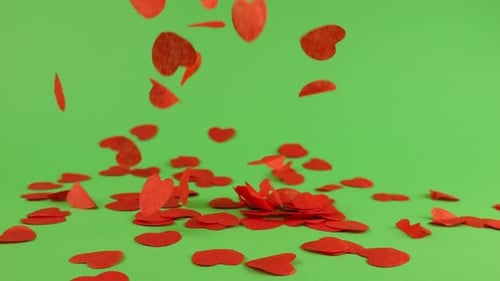 Falling heart-shaped confetti on a green background.