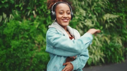Smiling girl walks in city park listening to music on headphones and dancing