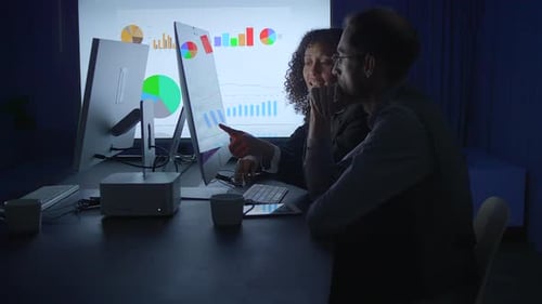 Two Adults Reviewing Data at Night in Office