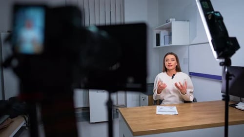Woman in white sweater sitting at desk talking to camera. Footage of the video for a blog.