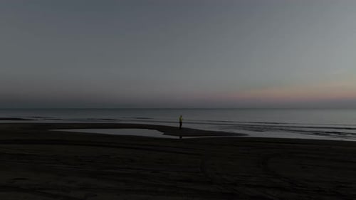 Eine Person steht bei Sonnenuntergang alleine an einem Strand. Ruhige Wellen und eine friedliche Atmosphäre