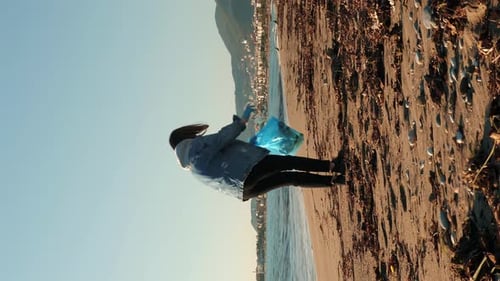 Female volunteer picking up garbage on beach. Vertical video.