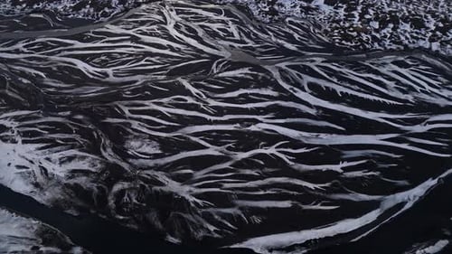 Dramatic aerial drone shot of a river winding through volcanic terrain in Iceland, with