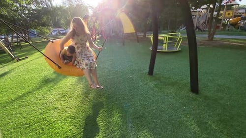 A happy child rides together with his mother on a swing. Toddler baby and his mom swinging on the pl