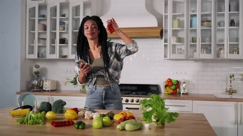 Woman Looks at Fresh Vegetables and Cellphone in Kitchen