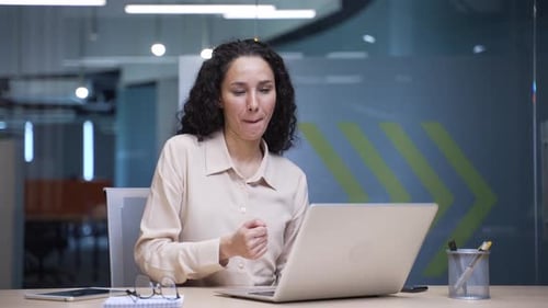 Happy businesswoman finished work on laptop and dances while sitting at workplace in business office