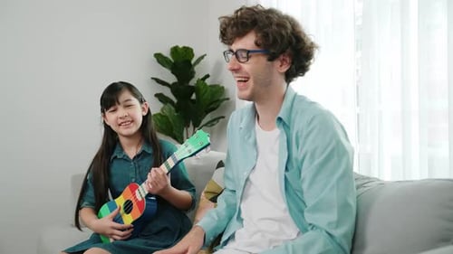 Back view of father looking at smart daughter playing ukulele warmly. Pedagogy.
