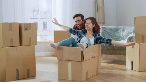 Young Couple Moving Into New Apartment, Boyfriend Drives Girlfriend in Cardboard Box, She imitates