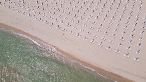 A Sandy Beach Stretches Along the Seaside Adorned with Empty Sun Loungers Aerial View