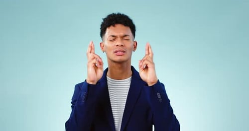 Hope, face and man with fingers crossed, prayer and anxiety in studio for lottery