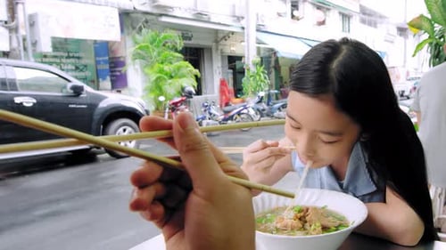 Asian father and daughter enjoying traditional noodles at bangkok street food stall