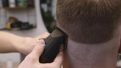 Friseur mit Trimmer schneidet männlichen Kunden im Geschäft die Haare