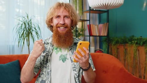 Young Man Celebrates Success on Smartphone at Home