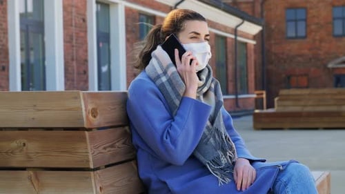 Young woman in protective mask calls on smartphone during coronavirus pandemic in city