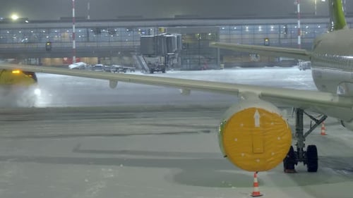 Snow being cleaned in airport - zoomed in shoot above airplane wing - building suspense.